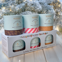 Load image into Gallery viewer, Holiday Hot Chocolate Collection with Classic Dark, Peppermint, and Classic Milk cylinders on a boxed set by a frosted tree