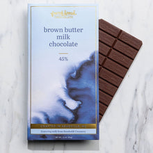 Load image into Gallery viewer, Brown Butter Milk Chocolate 45% bar in watercolor packaging with an unwrapped milk chocolate bar behind it on marble.