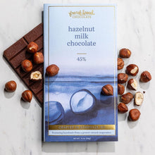 Load image into Gallery viewer, Hazelnut Milk Chocolate 45% bar in watercolor wrapper over an unwrapped bar, with whole and halved hazelnuts alongside.