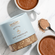Load image into Gallery viewer, Mocha Hot Chocolate Mix cylinder with coffee bean pattern beside mugs of hot chocolate and a spoonful of mix on marble