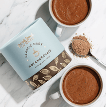 Load image into Gallery viewer, Classic Dark Hot Chocolate Mix cylinder on marble beside two full mugs and a spoonful of cocoa mix

