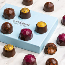 Load image into Gallery viewer, Signature Collection bonbons arranged on a blue French Broad Chocolates box, one bitten open to show a soft chocolate center.
