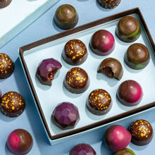 Load image into Gallery viewer, Open box of Dark Chocolate Collection bonbons with gold-speckled and jewel-toned shells, two bitten open, on a blue backdrop.
