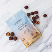 Load image into Gallery viewer, Milk Chocolate Caramelized Hazelnuts pouch on marble, loose chocolate-covered hazelnuts around it, one split open
