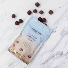 Load image into Gallery viewer, Pale blue pouch of dark chocolate covered espresso beans on white marble with beans scattered around the bag.
