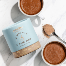 Load image into Gallery viewer, Classic Milk Hot Chocolate Mix cylinder on marble with two mugs of creamy hot chocolate and a spoon of mix
